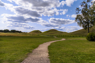 Dirt path snakes its way through the field to the royal burial mounds in Gamla Uppsala, Sweden under a blue sky with fluffy white clouds