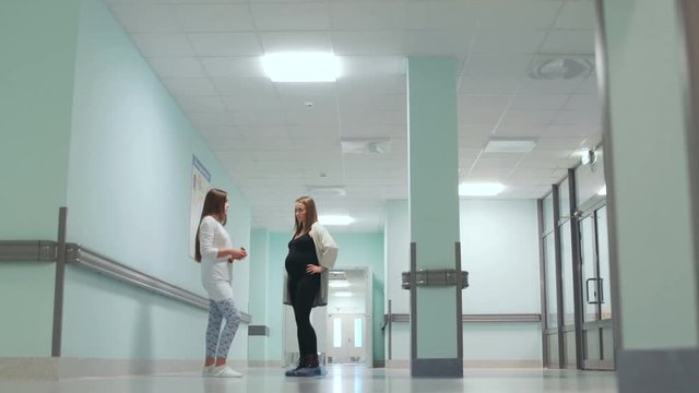 Dialogue between a pregnant woman and a female doctor in the corridor of the hospital. Preparation for childbirth. Consultation on childbirth. Smiling people. Slider. Horizontal movement of the camera