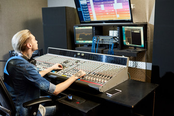 Serious busy handsome hipster male audio engineer with headphones on neck working on sound control...