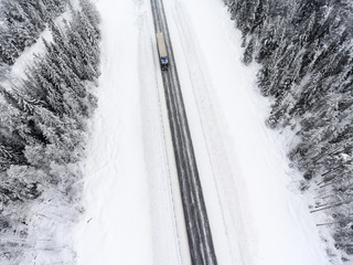 White semitrailer truck fast driving toward on slippery winter asphalt highway, aerial view from drone