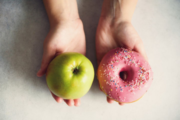 Young woman in white T-shirt choosing between green apple or junk food, donut. Healthy clean detox...