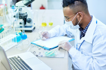 Side view portrait of young Middle-Eastern scientist working with petri dish studying chemical...