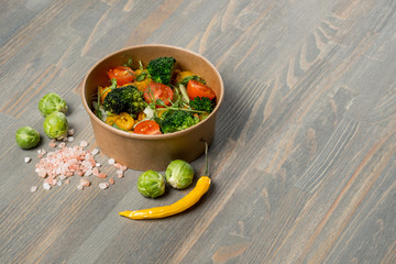 Fast food concept - vegetarian mix salad in lunch box on wooden background with vegetables ingredients.