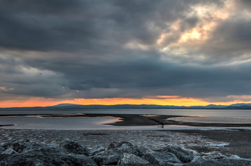 Obraz premium The sun sets on fire above the hills and mountains of the Lake District on the other side of Morecambe Bay, Lancashire, England