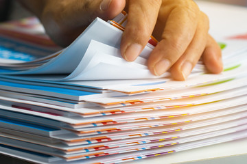 Businessman hands searching unfinished documents stacks of paper files on office desk for report...