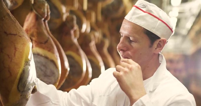 In a ham factory, a man in charge of quality control walks between the hams and controls, the perfume and the certified Italian quality. Concept of: tradition, Italy, food, ham