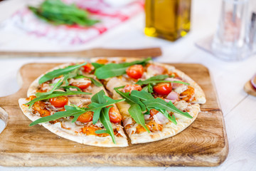 hot fresh homemade traditional italian pizza with cheese, tomatoes and rocked salad on wooden cooking table. wallpaper for pizzeria and food concept. soft focus