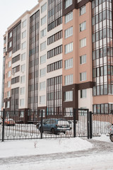 A panel house in winter, a multi-story building in a new microdistrict. Parked cars at the fence in the snow.