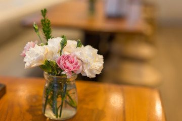 A vase, glass of flower with cute pink and white Paeonia flower on the wooden table in the cafe with classic and warm tone decoration