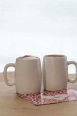 Two white cups of coffee with a valentine on a light background. Design card for Valentines day