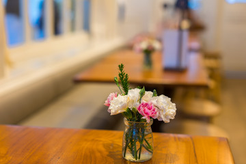 A vase, glass of flower with cute pink and white Paeonia flower on the wooden table in the cafe with classic and warm tone decoration