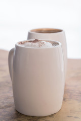 Two white cups of coffee stand on a world map against a light background