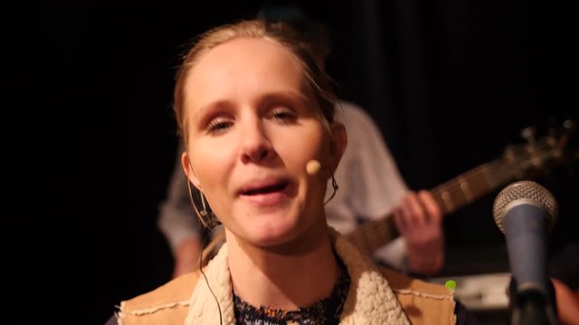 Young blond woman singing into the camera during concert.