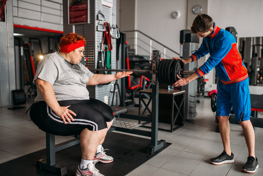 Fat woman using barbell, training with instructor