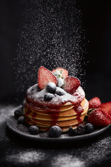  Pancakes close up, with fresh strawberry, blueberries, mint and jam on a black background