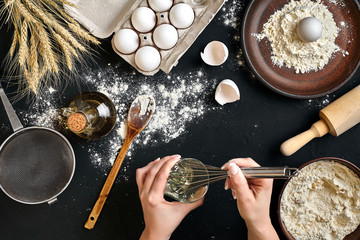 Whipping eggs. Chef hands close-up whisk eggs on a black background. View from above.