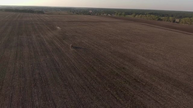 Aerial view flying over the top of a combine harvester and tractor in a field