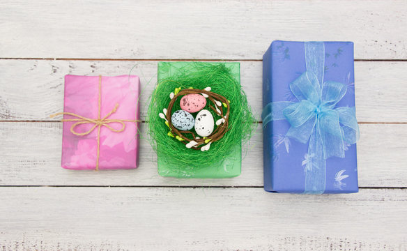 Easter concept- easter colored eggs in the nest , gift boxes  on white wooden background.Greeting card template