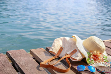 Summer accessories with woman bag, hat and sunglasses placing on the wooden path with the sea water background