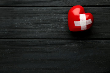 Red heart with adhesive bandage on black wooden table