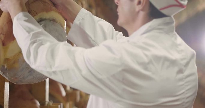 In a ham factory, a man in charge of quality control walks between the hams and controls, the perfume and the certified Italian quality. Concept of: tradition, Italy, food, ham