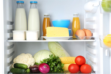 Open fridge full of vegetables and bottles of milk and juice