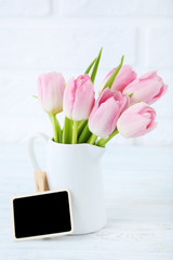 Bouquet of tulips in jug on brick wall background