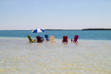 Holidays vacation symbolic seascape, set of different sun deck chairs and sun umbrella on the shallow turquoise waters, beach sandbar island wildlife refugee which appear during low tide