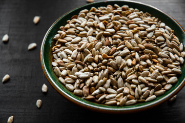 Ruddy peeled sunflower seeds in a bowl on dark wooden background with copy space.