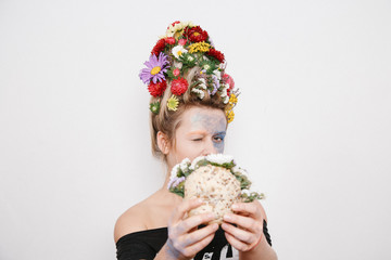 A young woman with flowers on her head and hands. Spring image with flowers. The girl and the blooming haircuts and brocade on her face.