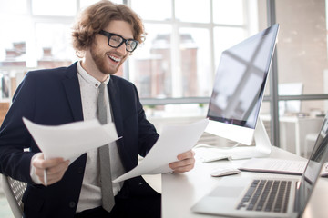 Happy young financier reading documents or new contracts in office