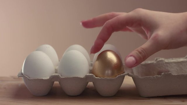 womnan hand open an egg pack with a six eggs and take away one golden egg from another white eggs
