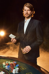 A man in a business suit standing near the game table. Male player. Passion, cards, chips, alcohol, dice, gambling, casino - it is as male entertainment.
