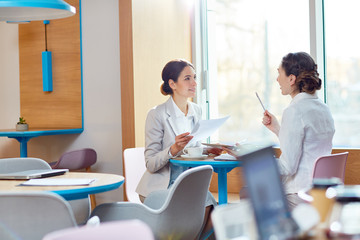 Two young agents sitting in cafe, discussing papers and organizing work
