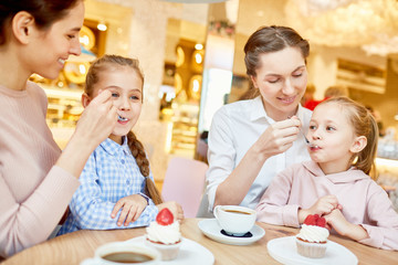 Obraz na płótnie Canvas Two careful mothers feeding their little daughters with tasty dessert while spending time in cafe
