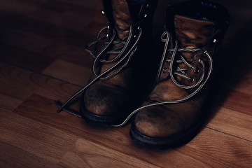 Pair of warn out boots with shoelaces on a wooden floor