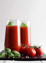 Tomato juice in a glass with a cherry and basil on a light background