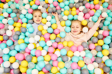 Fototapeta na wymiar Two little cheerful girls having fun in heap of inflatable balls of various colors
