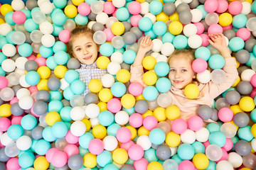 Fototapeta na wymiar Two adorable friendly girls playiing in heap of colorful balloons at birthday party