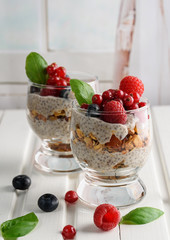 Two glasses of chia pudding with fresh strawberries, raspberries and blueberries. Basket with berries. On a wooden light background.