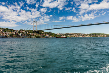 Fototapeta na wymiar View of Fatih Sultan Mehmet Bridge which is localed on Bosphorus strait . Ships passing through bridge connecting Europe and Asia. Sunny day with background of cloudy blue sky. Istanbul. Turkey.