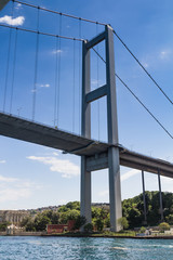 View of the First Bosporus Bridge. Ships passing through bridge connecting Europe and Asia. Sunny day with background of cloudy blue sky. Istanbul. Turkey.