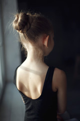 Fototapeta na wymiar Back of a little adorable young ballerina in black sportwear in sunlight