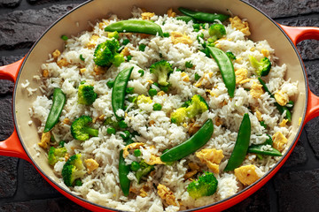 Fried rice with vegetables, broccoli, peas and eggs served in a pan. healthy food