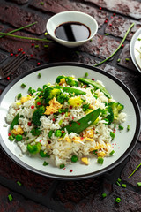 Fried rice with vegetables, broccoli, peas and eggs in a plate. soy sauce. healthy food