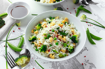 Fried rice with vegetables, broccoli, peas and eggs in a white bowl. soy sauce. healthy food