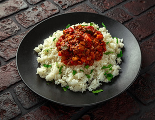 Homemade beef mince and vegetable casserole served with rice on black plate.