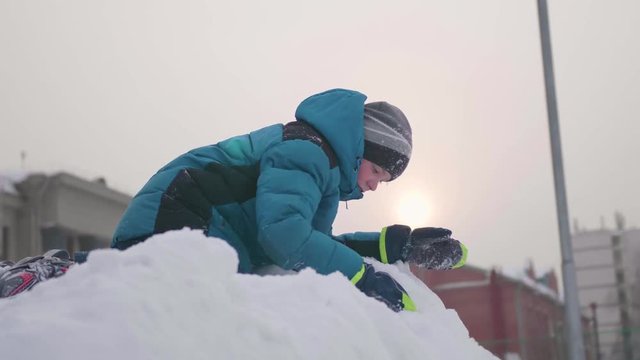 A teenager on top of a snowy mountain, throws snow and laughs . Sunny frosty day. Fun and games in the fresh air.