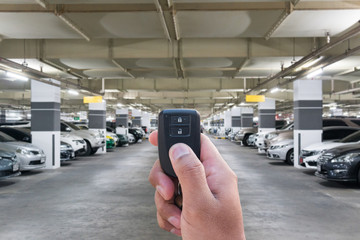 Male holding car keys remote with car on Parking garage In the mall for background.
