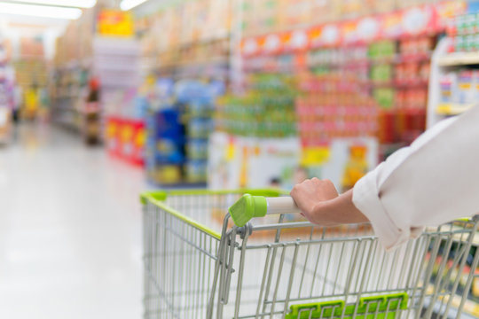 Woman pushing shopping cart in supermarket store abstract blur background with shopping cart, Supermarket aisle with empty shopping cart